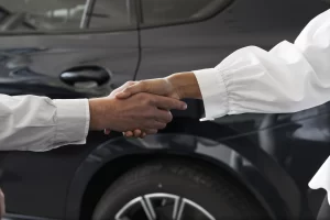 Woman and man shaking hands in front of car representing transparent pricing and no hidden fees